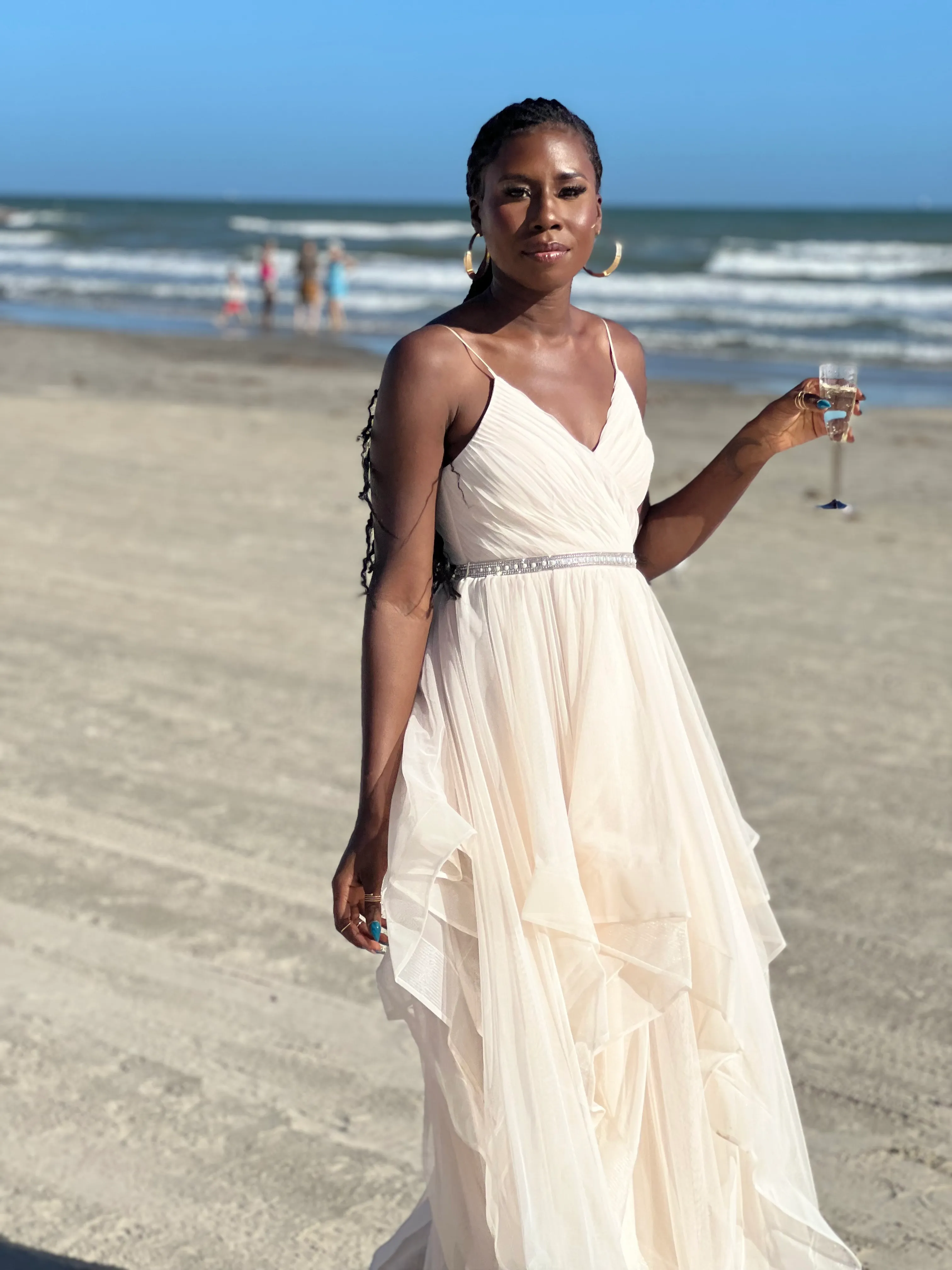 Nala walking on the beach in a white dress holding a glass of champagne
