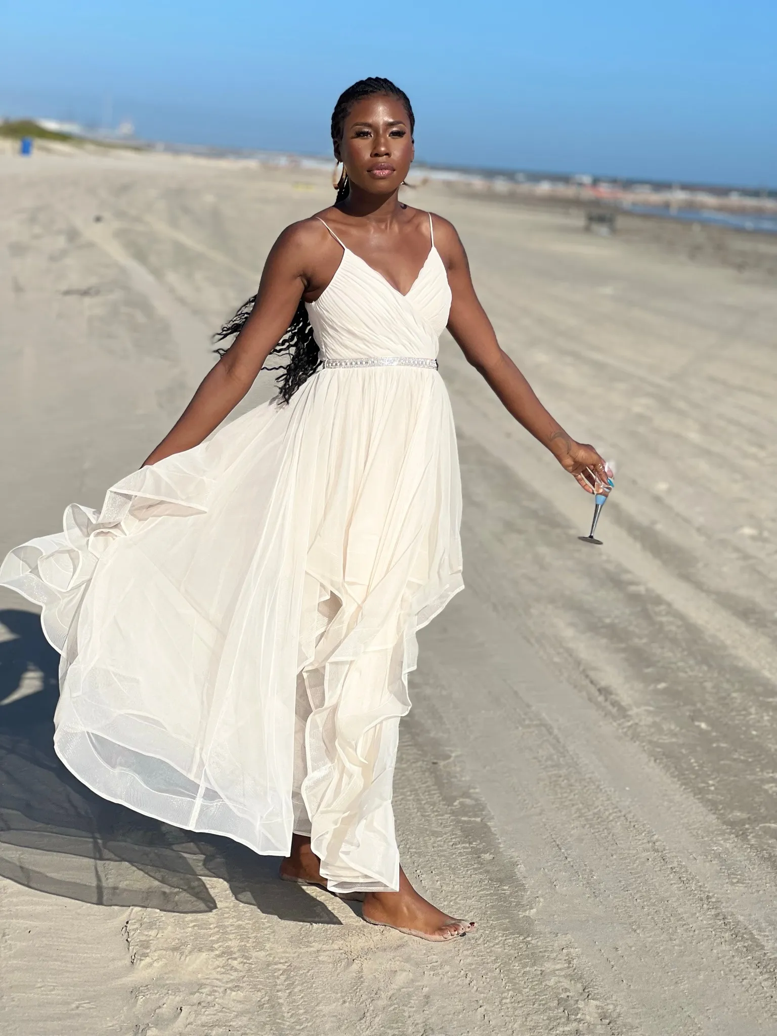 Nala walking on the beach in a white dress holding a glass of champagne