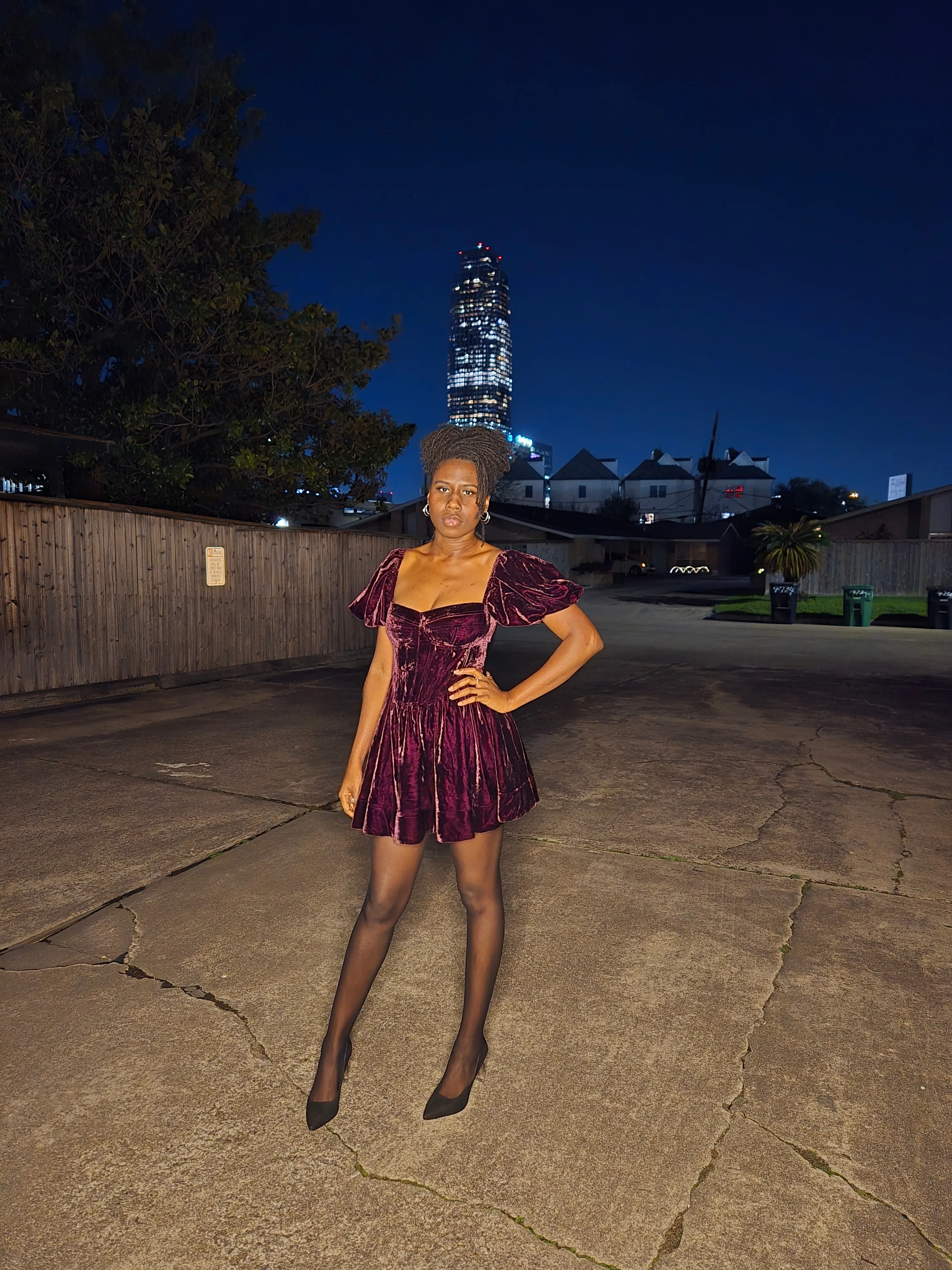 Nala in a burgundy velvet dress, hand on hip, at night