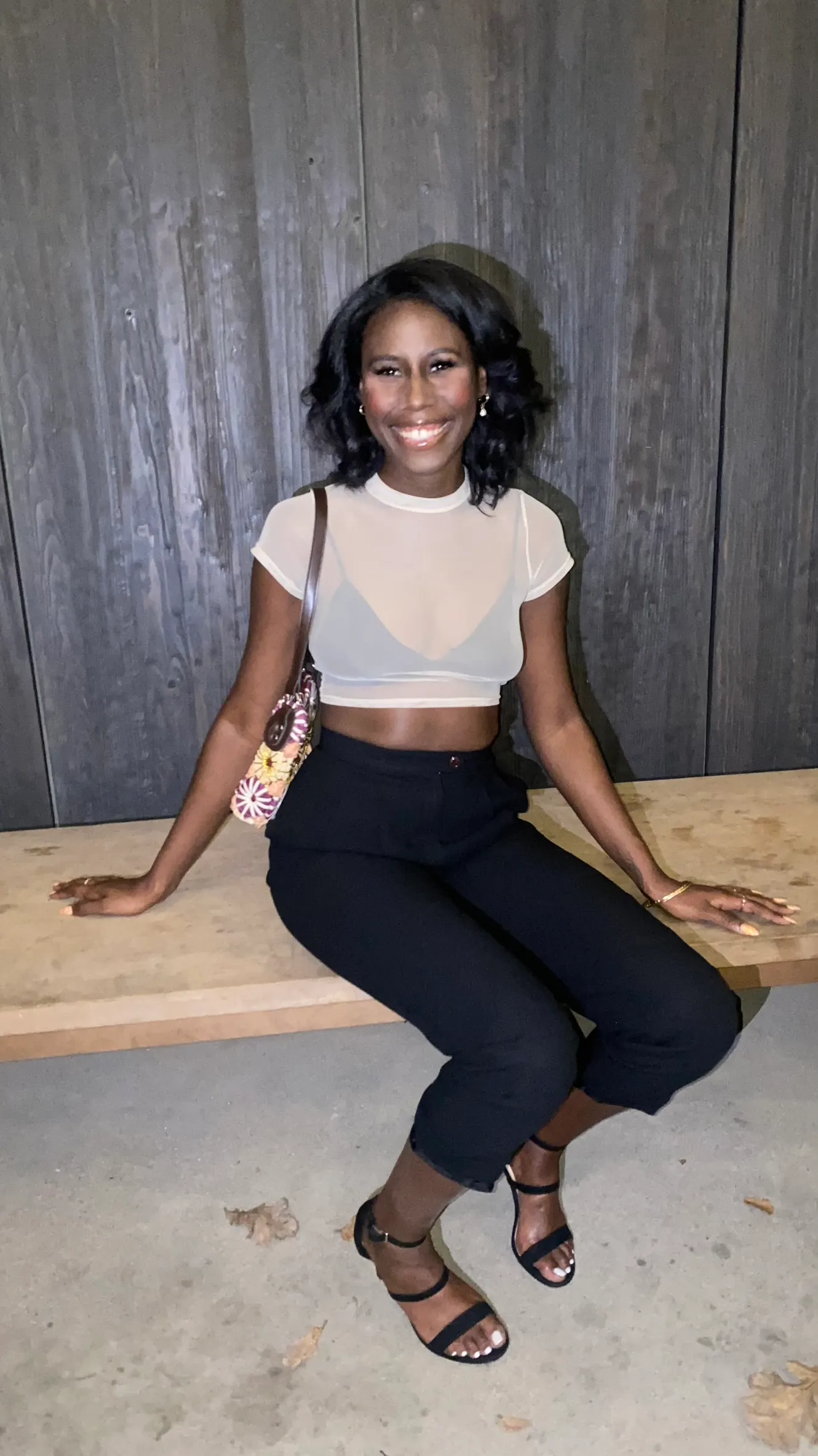 Nala smiling, seated on a bench in a white mesh crop top