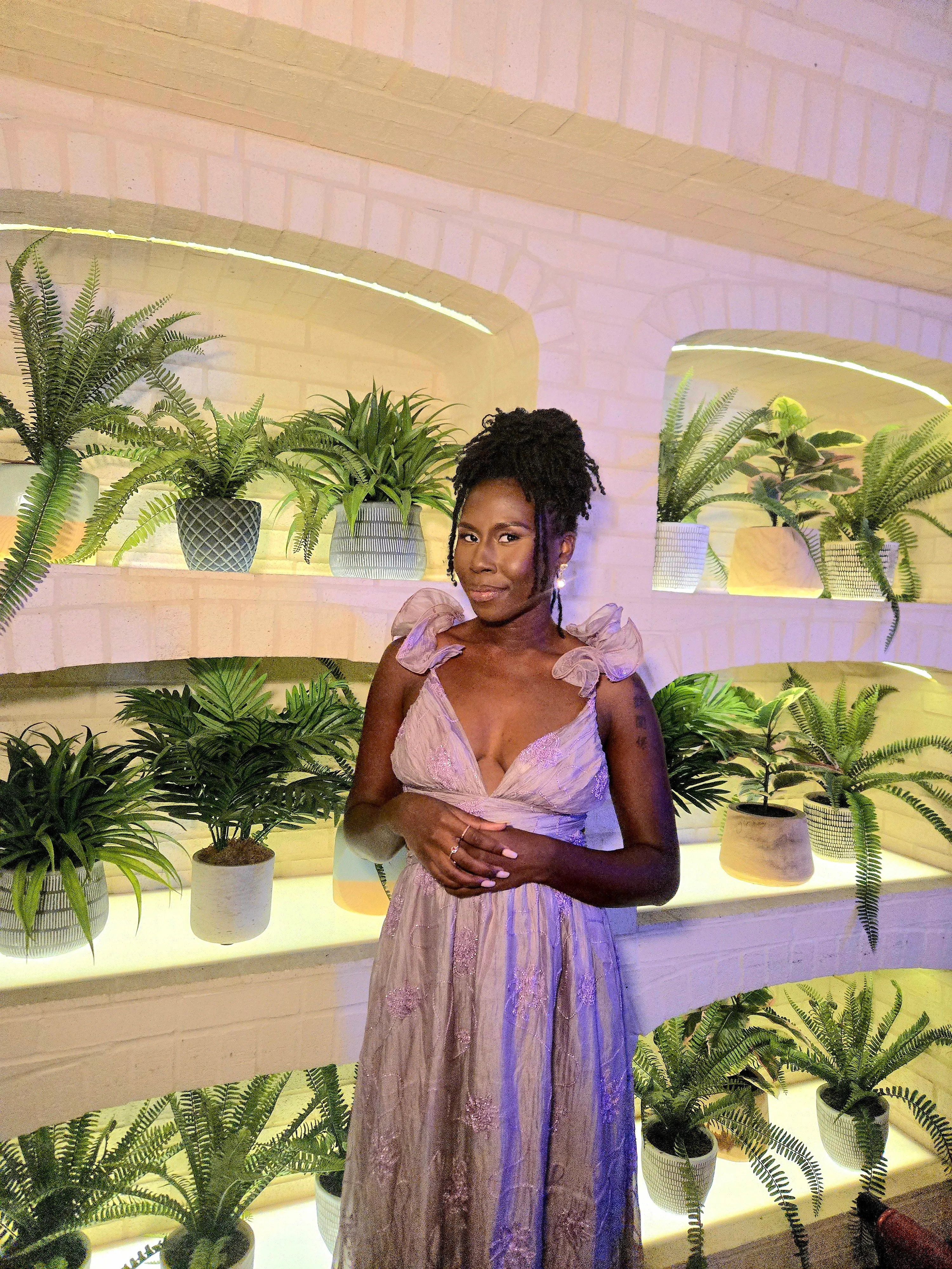 Nala in a lavender tulle gown in front of a wall of ferns