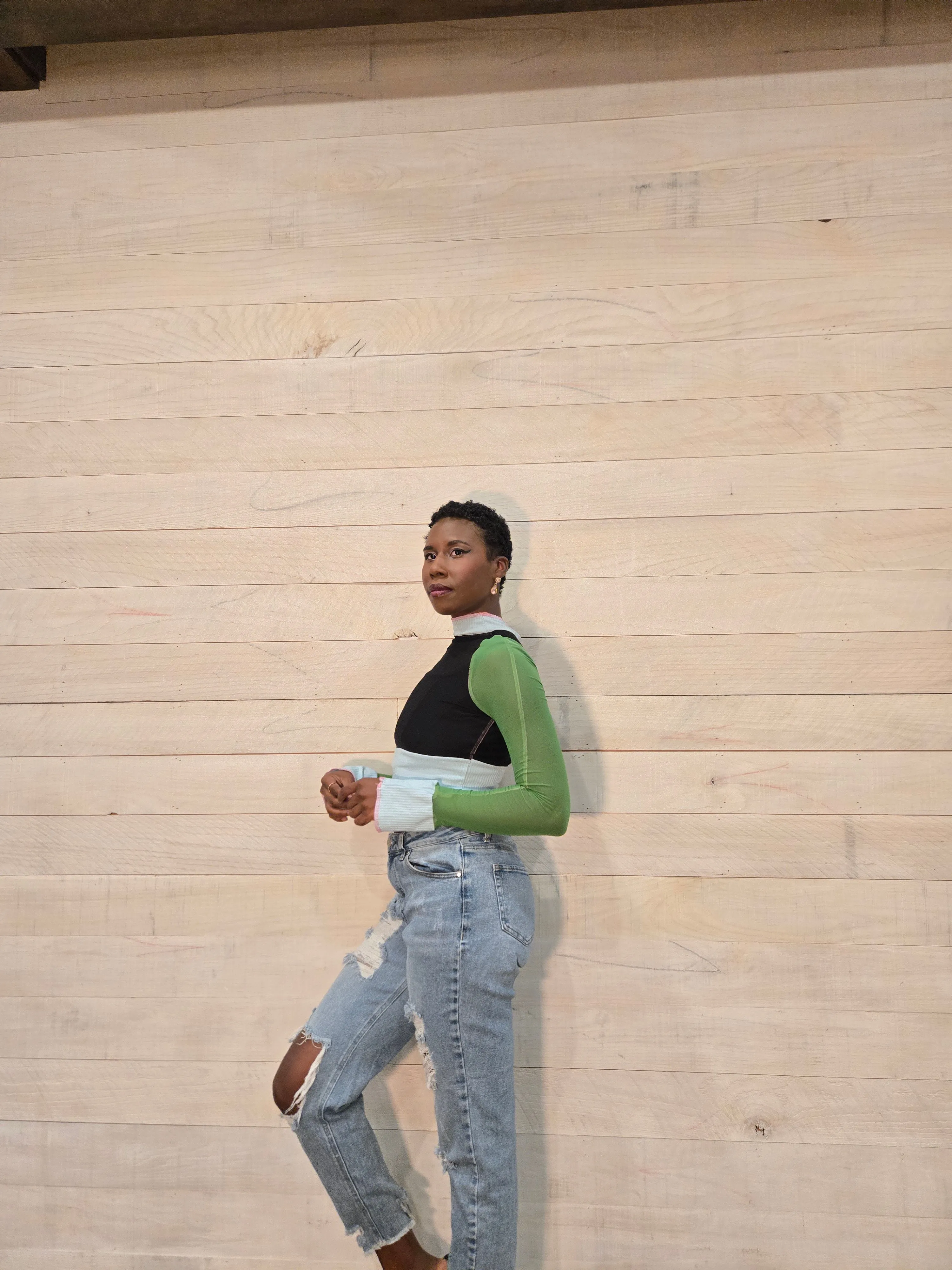 Nala in profile in a green long-sleeve top against a wood wall