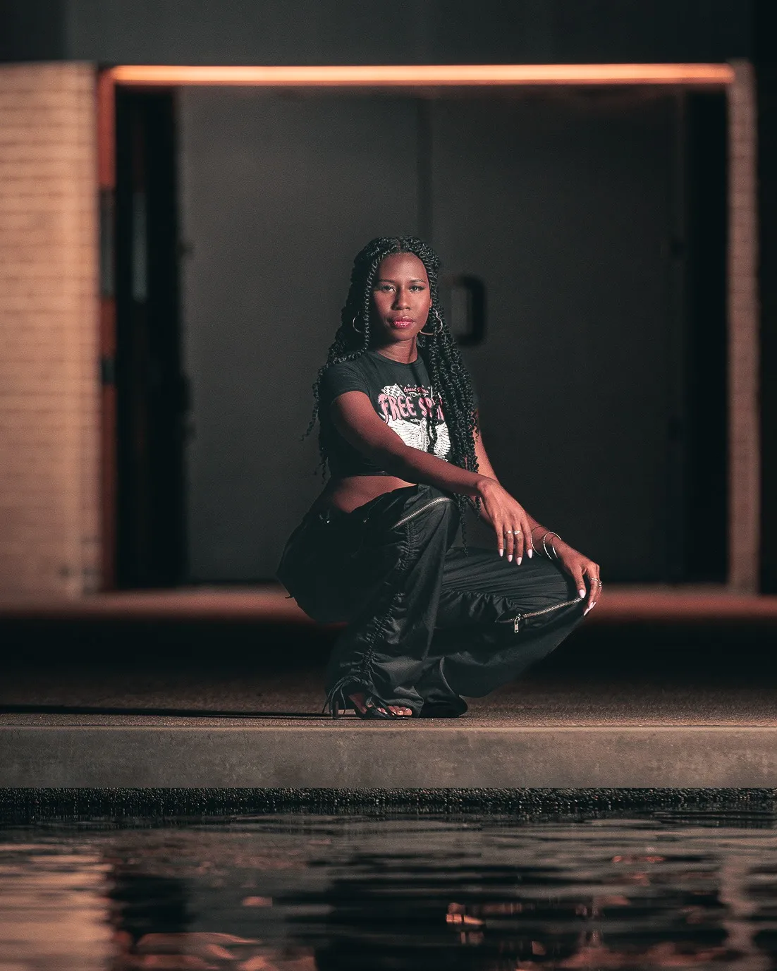 Nala crouching poolside at night in a graphic tee and cargo pants