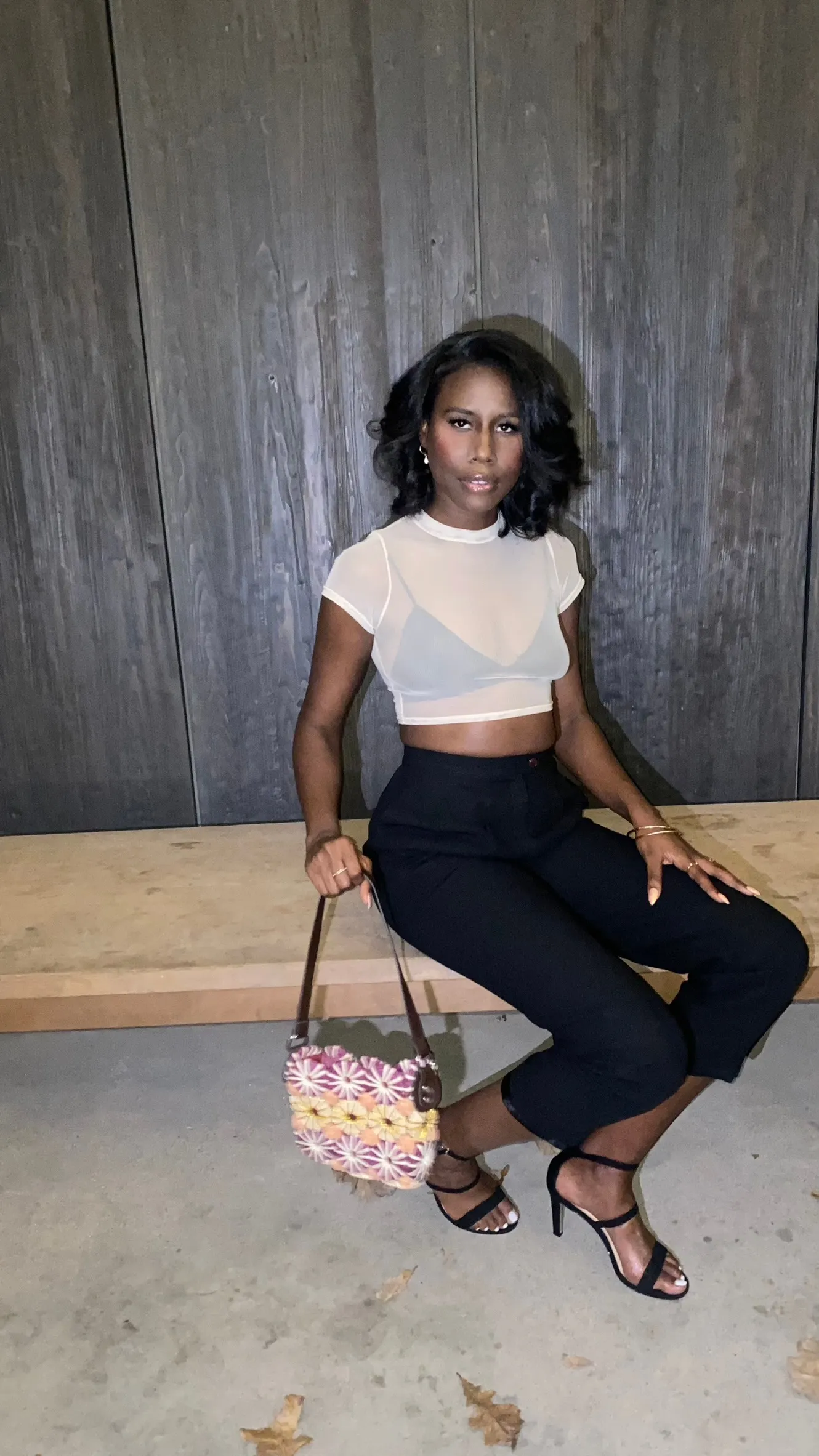Nala seated in a sheer white crop top with a woven bag